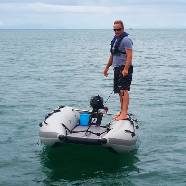 Man standing on an inflatable "Takacat" boat with a motor in calm water